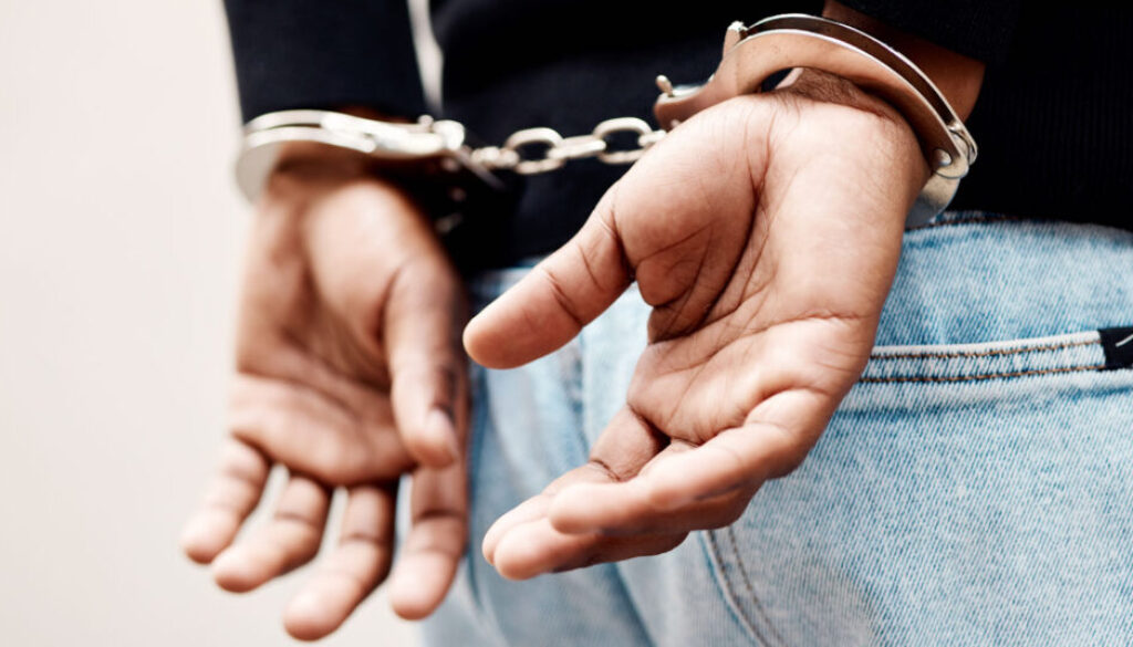 Back, arrest and handcuffs with a man suspect of a crime by law enforcement closeup on a gray background. Security, jail or prison with a male criminal handcuffed from behind for legal justice