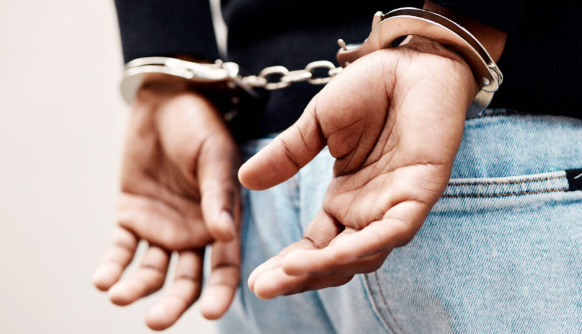 Back, arrest and handcuffs with a man suspect of a crime by law enforcement closeup on a gray background. Security, jail or prison with a male criminal handcuffed from behind for legal justice