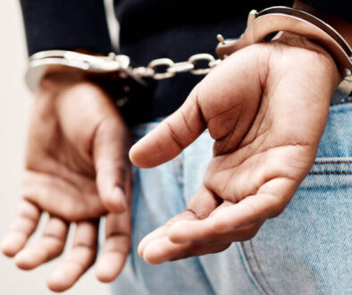 Back, arrest and handcuffs with a man suspect of a crime by law enforcement closeup on a gray background. Security, jail or prison with a male criminal handcuffed from behind for legal justice