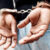 Back, arrest and handcuffs with a man suspect of a crime by law enforcement closeup on a gray background. Security, jail or prison with a male criminal handcuffed from behind for legal justice